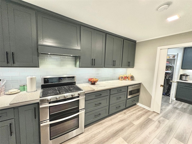 kitchen featuring gray cabinets, backsplash, light hardwood / wood-style floors, stainless steel appliances, and light stone countertops