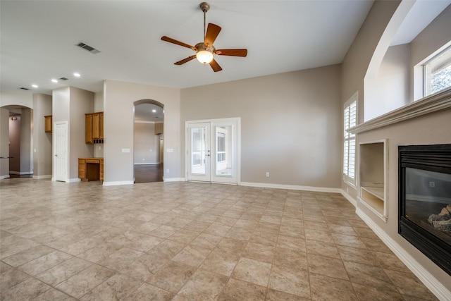 unfurnished living room featuring arched walkways, visible vents, a glass covered fireplace, ceiling fan, and baseboards