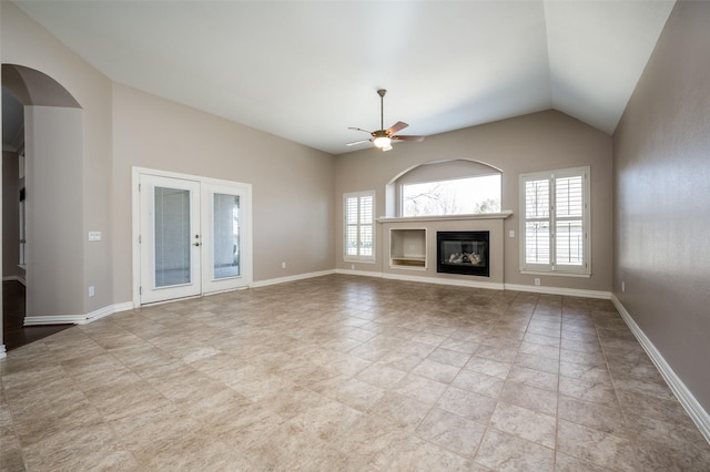 unfurnished living room featuring french doors, a ceiling fan, a glass covered fireplace, vaulted ceiling, and baseboards