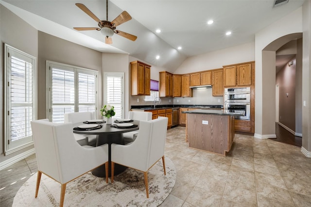 kitchen with a kitchen island, arched walkways, brown cabinets, and stainless steel double oven