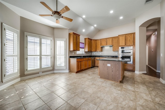 kitchen with appliances with stainless steel finishes, dark countertops, brown cabinets, and arched walkways