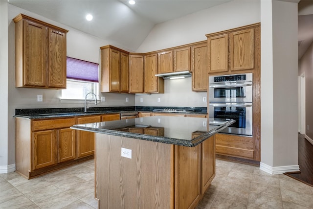 kitchen featuring under cabinet range hood, a sink, appliances with stainless steel finishes, a center island, and dark stone countertops