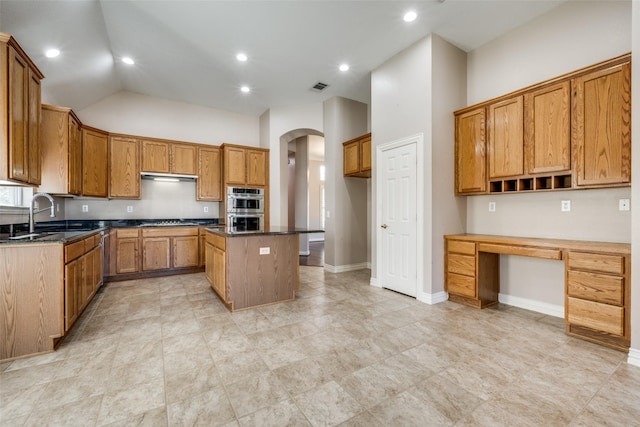 kitchen with double oven, a kitchen island, a sink, brown cabinets, and built in desk