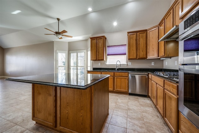 kitchen with a center island, brown cabinets, appliances with stainless steel finishes, vaulted ceiling, and a sink