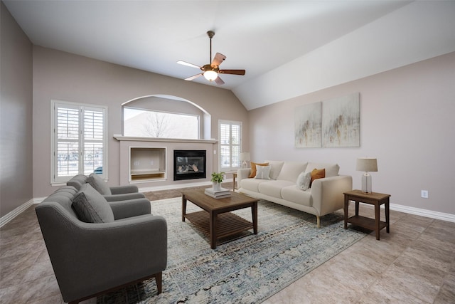 living area featuring a glass covered fireplace, vaulted ceiling, baseboards, and a ceiling fan