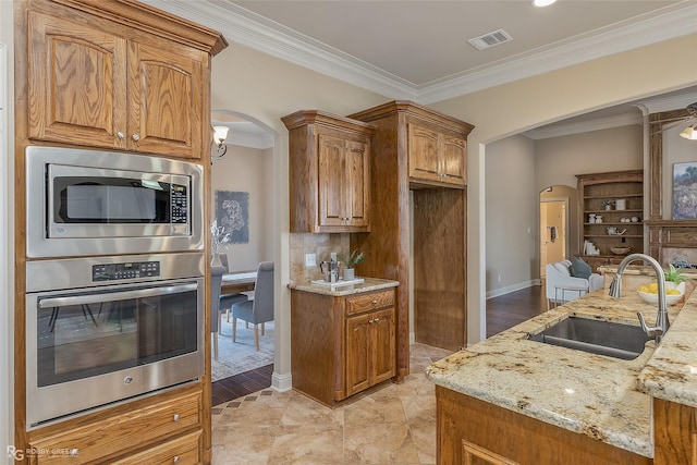 kitchen with light stone counters, stainless steel appliances, crown molding, and sink