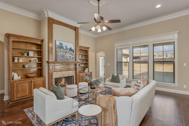 living room with a tiled fireplace, crown molding, dark hardwood / wood-style floors, and ceiling fan