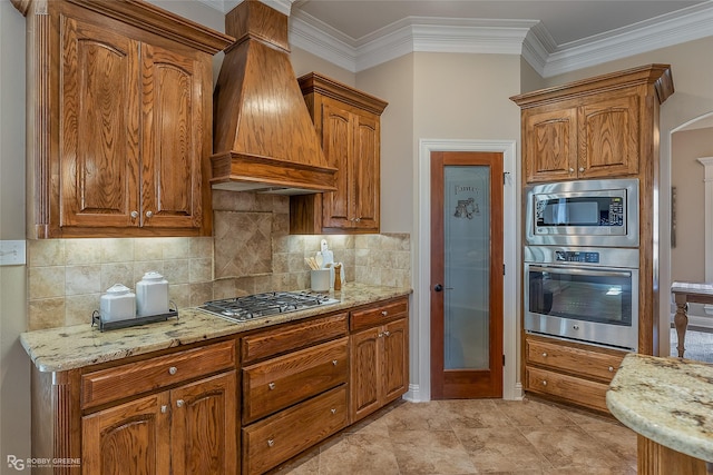 kitchen with appliances with stainless steel finishes, backsplash, custom exhaust hood, ornamental molding, and light stone counters