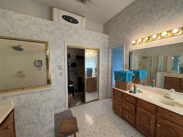 full bath featuring a stall shower, wallpapered walls, tile patterned floors, a textured ceiling, and vanity