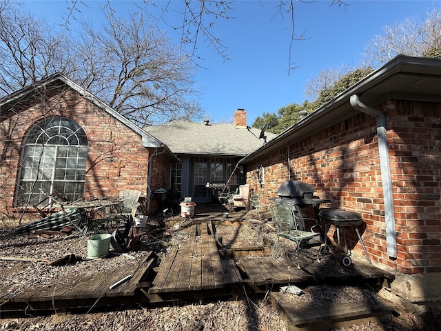 view of property exterior featuring brick siding, a chimney, a shingled roof, and a wooden deck