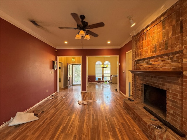 unfurnished living room with wood finished floors, visible vents, baseboards, a brick fireplace, and crown molding