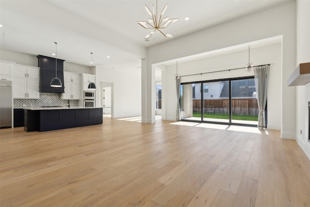 unfurnished living room featuring an inviting chandelier and light hardwood / wood-style flooring