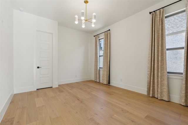 spare room featuring plenty of natural light, a chandelier, and light wood-type flooring