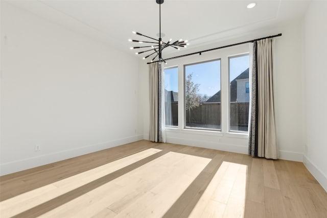 spare room with a notable chandelier and light wood-type flooring