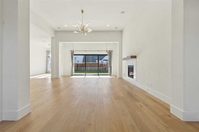 unfurnished living room featuring an inviting chandelier and light hardwood / wood-style flooring