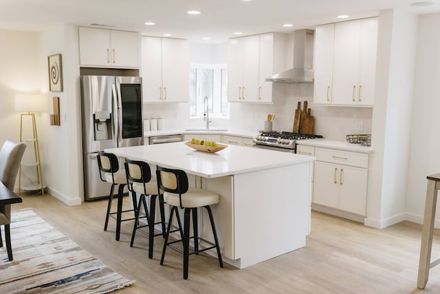 kitchen with wall chimney exhaust hood, sink, white cabinetry, appliances with stainless steel finishes, and a kitchen island