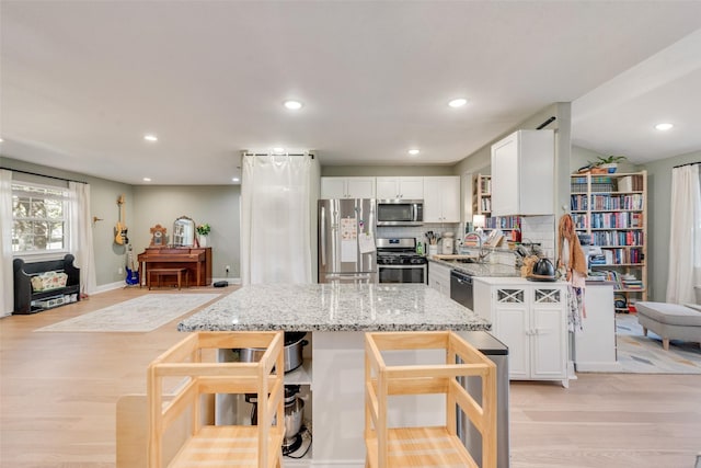 kitchen with white cabinets, stainless steel appliances, light stone countertops, light hardwood / wood-style floors, and backsplash