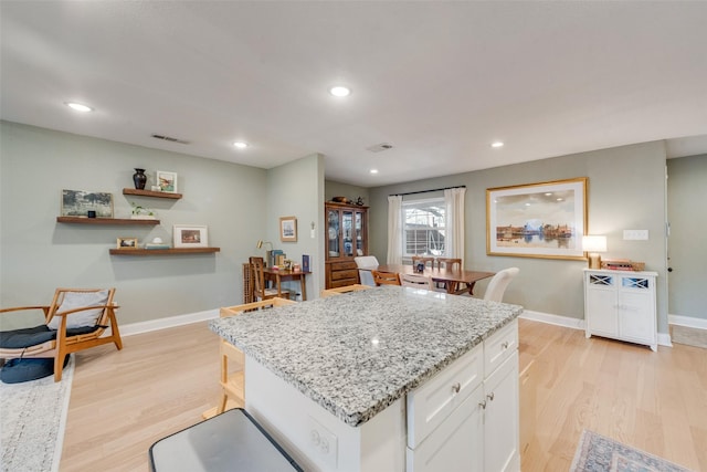 kitchen with a kitchen island, light stone countertops, light hardwood / wood-style flooring, and white cabinets