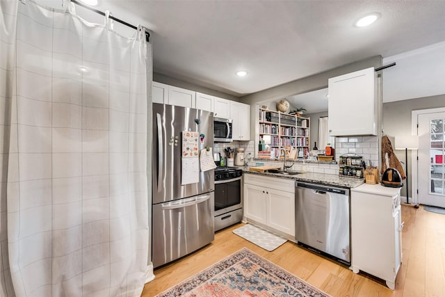 kitchen with sink, white cabinetry, light hardwood / wood-style flooring, stainless steel appliances, and decorative backsplash