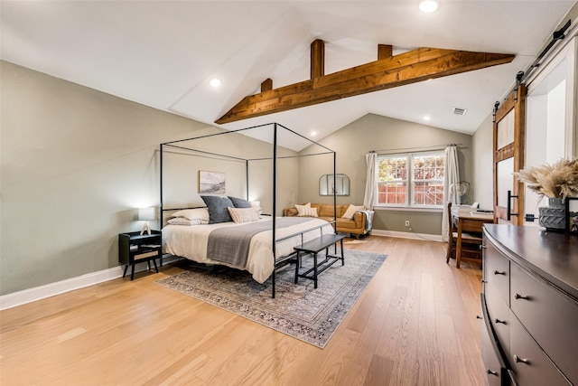 bedroom featuring a barn door, lofted ceiling with beams, and light hardwood / wood-style flooring