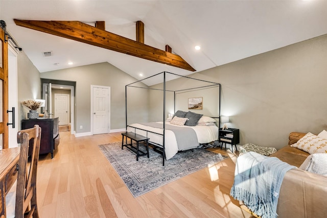 bedroom with lofted ceiling with beams, a barn door, and light hardwood / wood-style floors