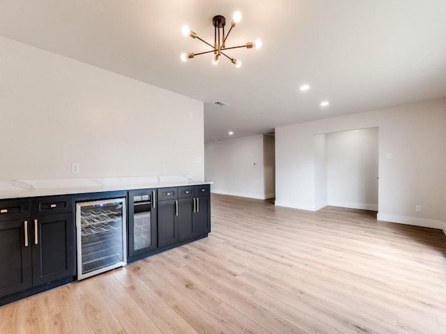 kitchen with light stone counters, a notable chandelier, beverage cooler, and light wood-type flooring