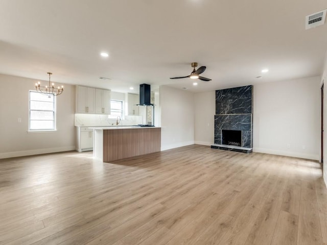 unfurnished living room featuring sink, ceiling fan with notable chandelier, a fireplace, and light wood-type flooring