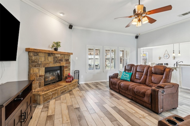 living room featuring crown molding, a stone fireplace, ceiling fan, and light wood-type flooring