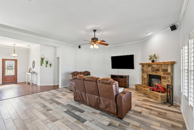 living room featuring crown molding, ceiling fan, a fireplace, and light wood-type flooring