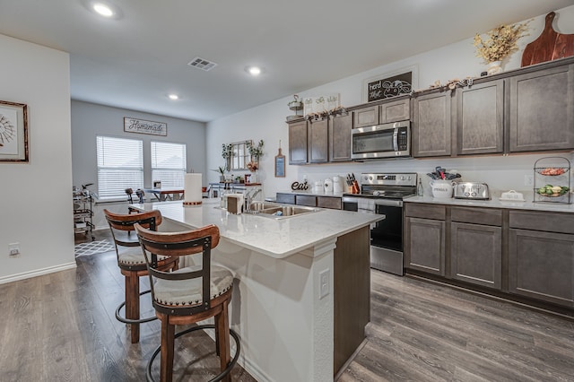 kitchen featuring an island with sink, appliances with stainless steel finishes, dark wood-type flooring, and dark brown cabinets