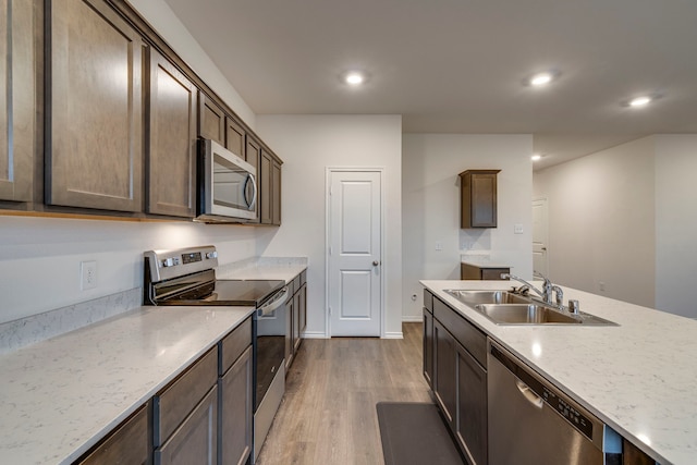 kitchen with dark brown cabinetry, sink, light stone counters, stainless steel appliances, and hardwood / wood-style floors