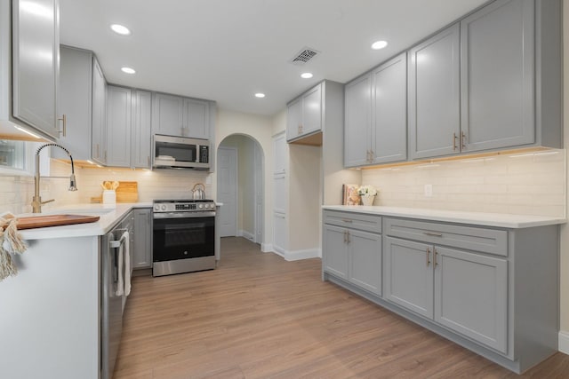 kitchen with gray cabinets, appliances with stainless steel finishes, sink, backsplash, and light hardwood / wood-style floors