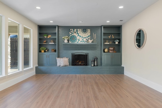 unfurnished living room with a brick fireplace, built in features, and light wood-type flooring