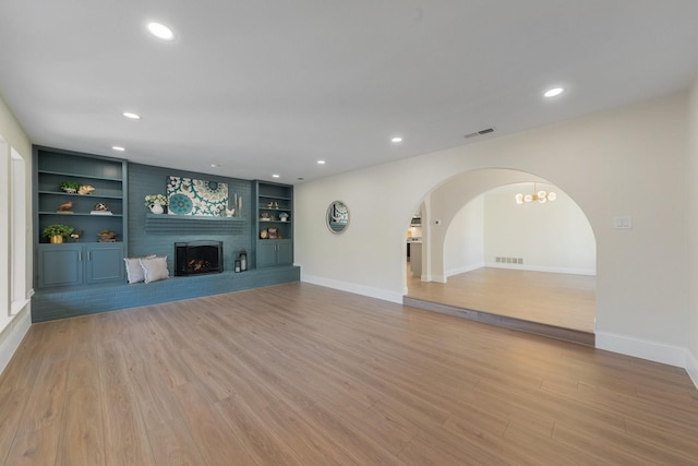 unfurnished living room featuring a brick fireplace, light hardwood / wood-style flooring, and built in features