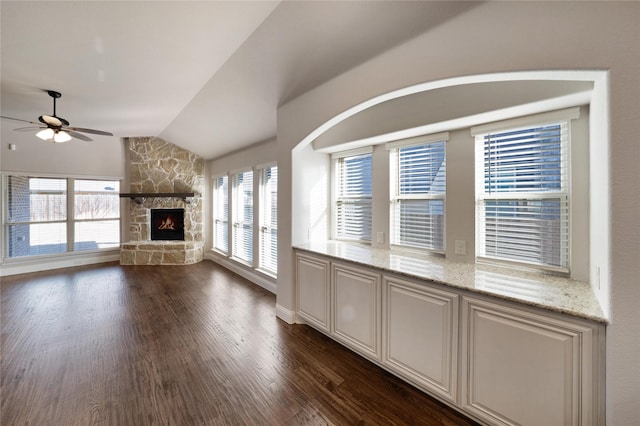 unfurnished living room featuring vaulted ceiling, a stone fireplace, ceiling fan, and dark hardwood / wood-style flooring