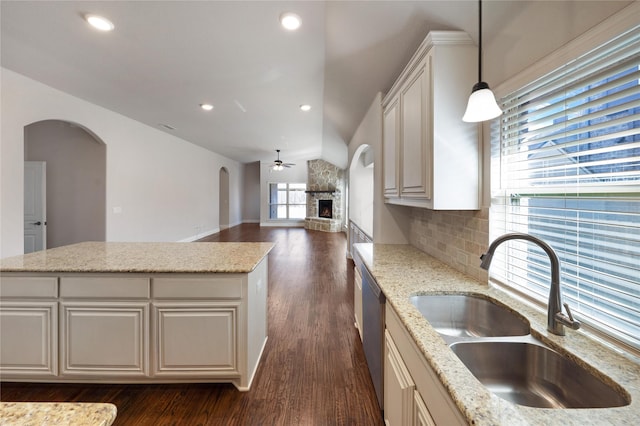 kitchen with a fireplace, decorative light fixtures, tasteful backsplash, sink, and light stone countertops