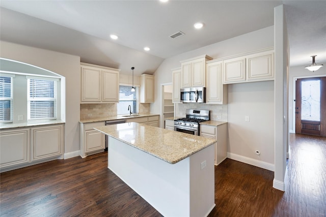 kitchen with appliances with stainless steel finishes, sink, hanging light fixtures, a center island, and light stone counters