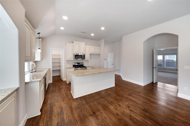 kitchen with pendant lighting, sink, appliances with stainless steel finishes, a center island, and light stone countertops