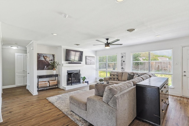 living room with ornamental molding, a tile fireplace, dark hardwood / wood-style floors, and ceiling fan