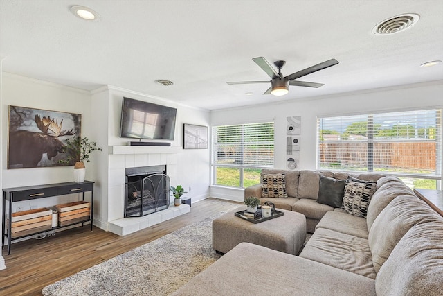 living room with hardwood / wood-style floors, ornamental molding, a tile fireplace, and ceiling fan