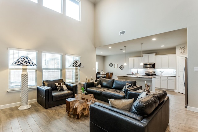 living room with a high ceiling, a wealth of natural light, and light hardwood / wood-style flooring