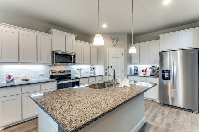 kitchen with sink, appliances with stainless steel finishes, a kitchen island with sink, hanging light fixtures, and white cabinets