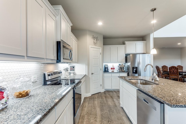 kitchen with sink, light hardwood / wood-style flooring, stainless steel appliances, white cabinets, and decorative light fixtures