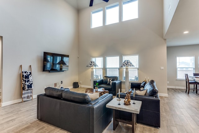 living room featuring ceiling fan, light hardwood / wood-style flooring, and a towering ceiling