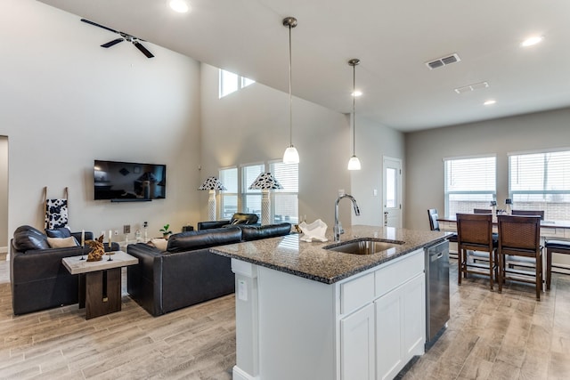 kitchen with pendant lighting, white cabinetry, sink, stainless steel dishwasher, and a center island with sink