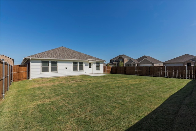 back of house featuring a shingled roof, a lawn, and a fenced backyard