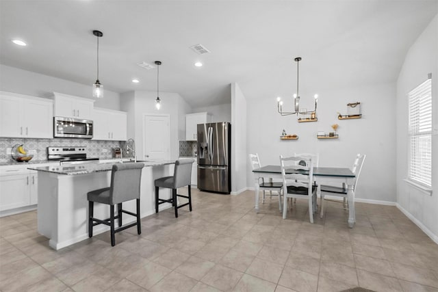 kitchen featuring a center island with sink, visible vents, appliances with stainless steel finishes, a kitchen breakfast bar, and a sink