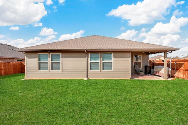 rear view of house with roof with shingles, a lawn, a patio area, and a fenced backyard