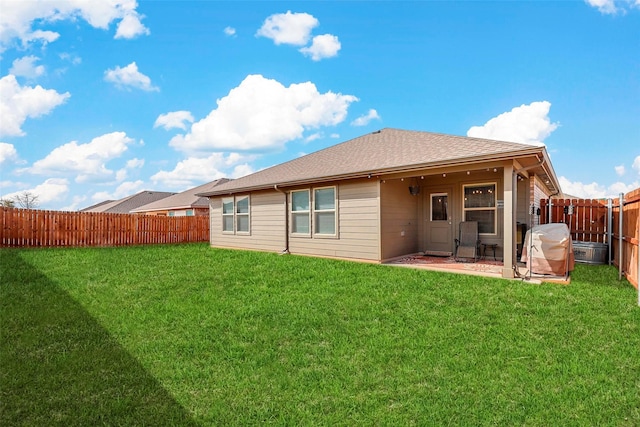 rear view of property featuring a fenced backyard, roof with shingles, and a yard