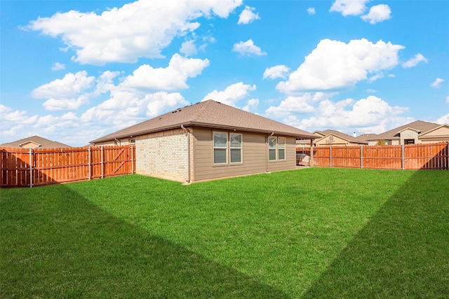 rear view of house featuring a fenced backyard, a lawn, and brick siding